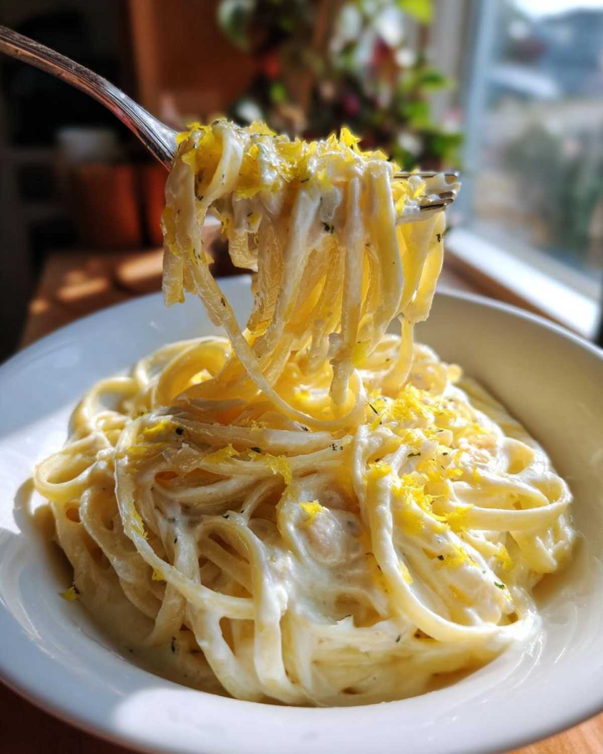 A fork lifts creamy white bean lemon pasta coated in sauce and topped with bright yellow lemon zest.