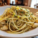 A close-up of One-Pot Creamy White Bean Lemon Pasta tossed with herbs and bright lemon zest in a white bowl.