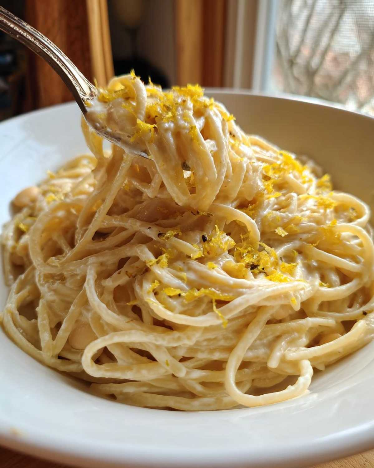 A fork lifts creamy strands of One-Pot Creamy White Bean Lemon Pasta topped with bright yellow lemon zest.