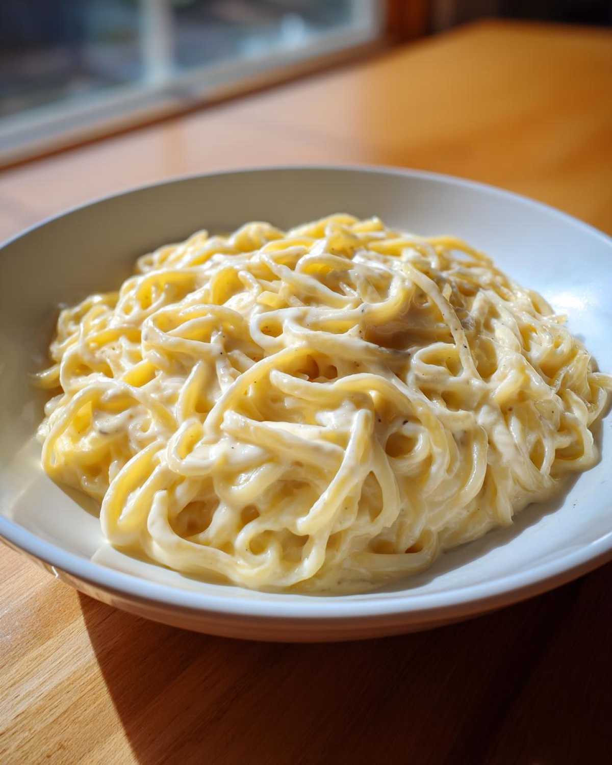 A bowl of spaghetti generously coated in rich, homemade Creamy Alfredo Sauce, highlighted by natural light.