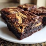 A fudgy square of peanut butter swirl brownies sits on a white plate, showing the rich chocolate interior and creamy swirl.