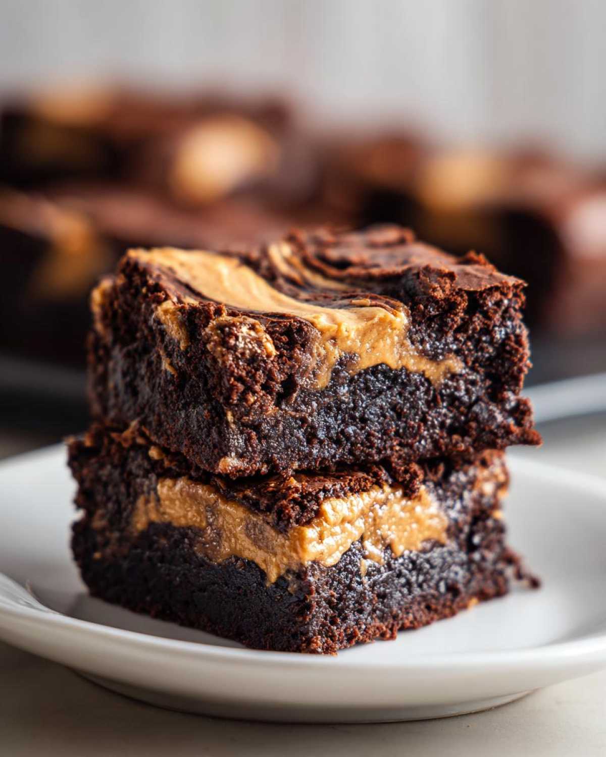Two rich, fudgy peanut butter swirl brownies stacked on a white plate.