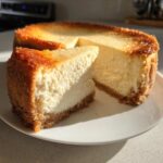A thick slice of perfectly baked cheesecake with a golden-brown top and graham cracker crust, showcasing the creamy texture of the ies filling.