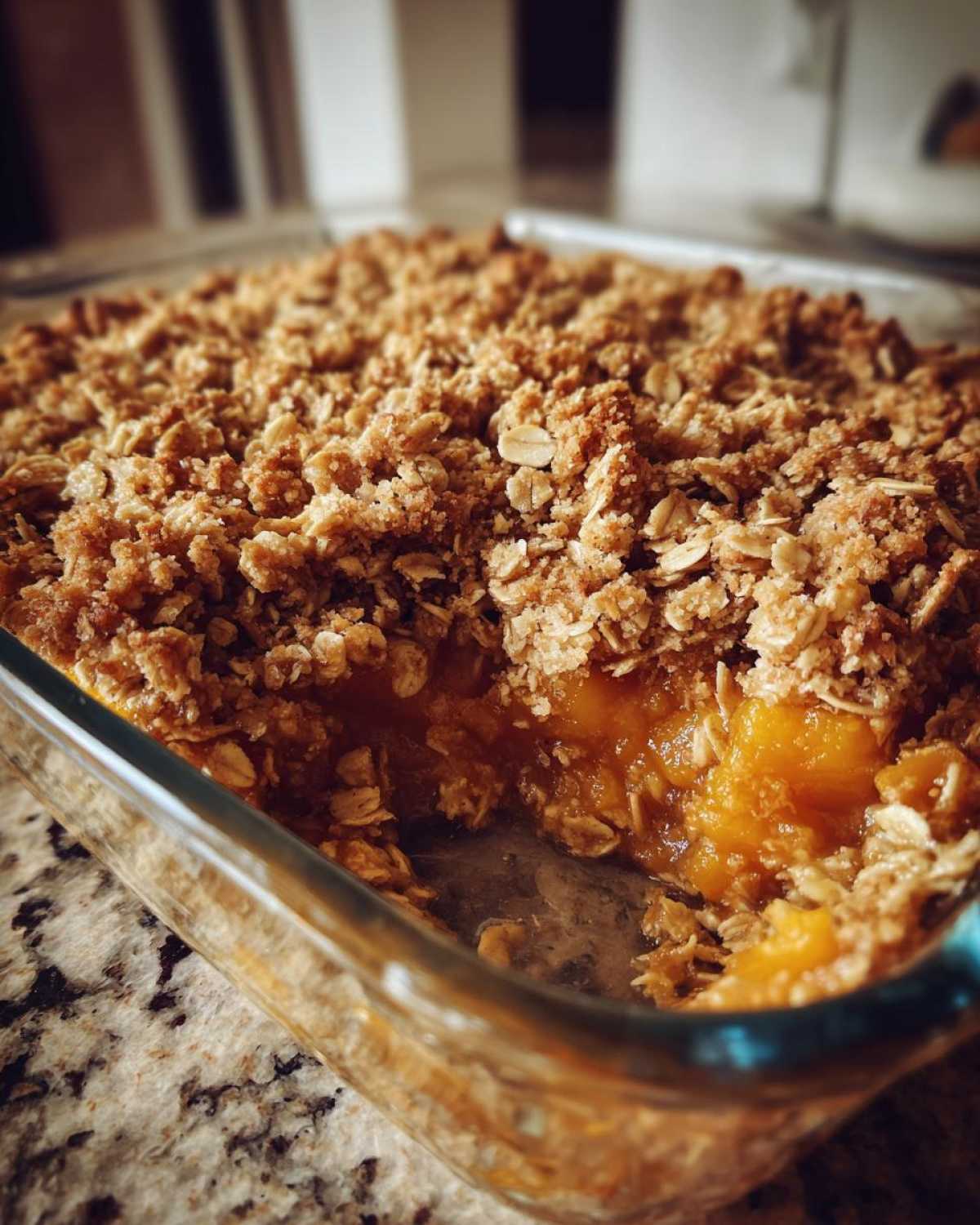A close-up view of a freshly baked pumpkin crisp in a clear glass baking dish, showing the thick oat topping and rich orange filling.
