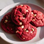 A stack of four vibrant red velvet cake mix cookies studded with white chocolate chips, resting on a white plate.