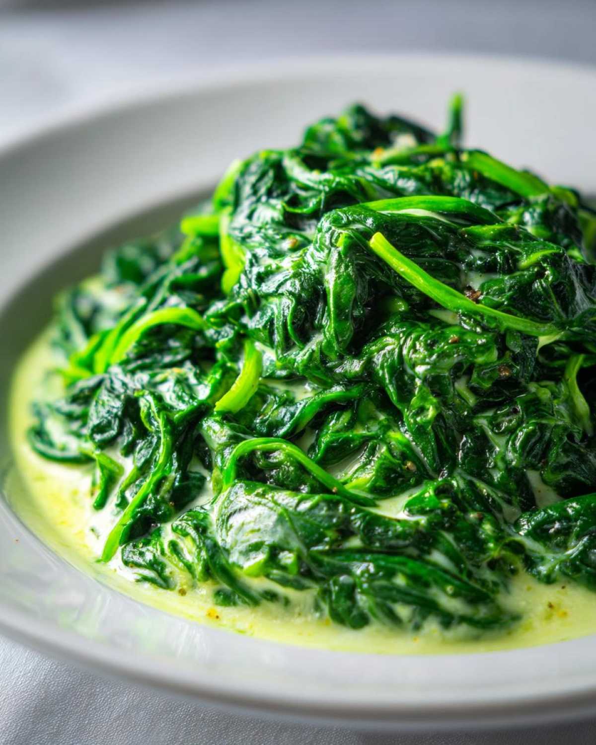 A close-up, vibrant shot of rich, dark green creamed spinach served in a white bowl.