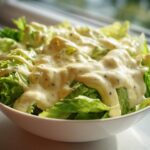 A bowl of fresh green lettuce generously topped with the Vegan Creamy Lemon Tahini Dressing.