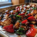 Close-up of glistening Sheet Pan Balsamic Strawberry Chicken with Spinach cooked on a metal baking sheet.