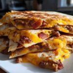 A stack of crispy, golden-brown Sheet Pan Breakfast Quesadillas cut into wedges, showing melted cheddar cheese and sausage filling.
