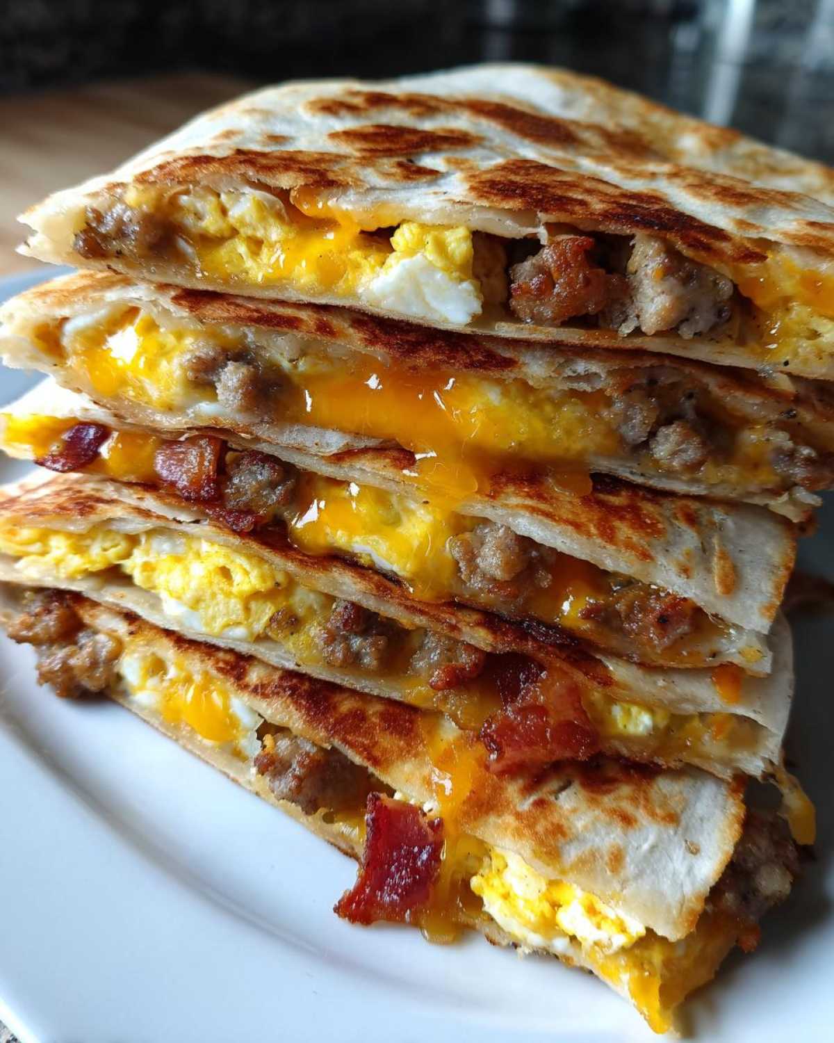 Close-up of stacked Sheet Pan Breakfast Quesadillas filled with scrambled eggs, sausage, bacon, and melted cheddar cheese.