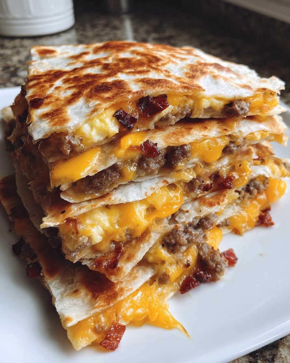 A tall stack of crispy, golden-brown Sheet Pan Breakfast Quesadillas filled with melted cheese, sausage, and bacon.