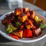 Close-up of glazed Sheet Pan Crispy Honey Mustard Tofu cubes served with roasted broccoli and red peppers on a white plate.