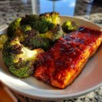 A close-up of Sheet Pan Honey Harissa Salmon with roasted broccoli florets on a white plate.