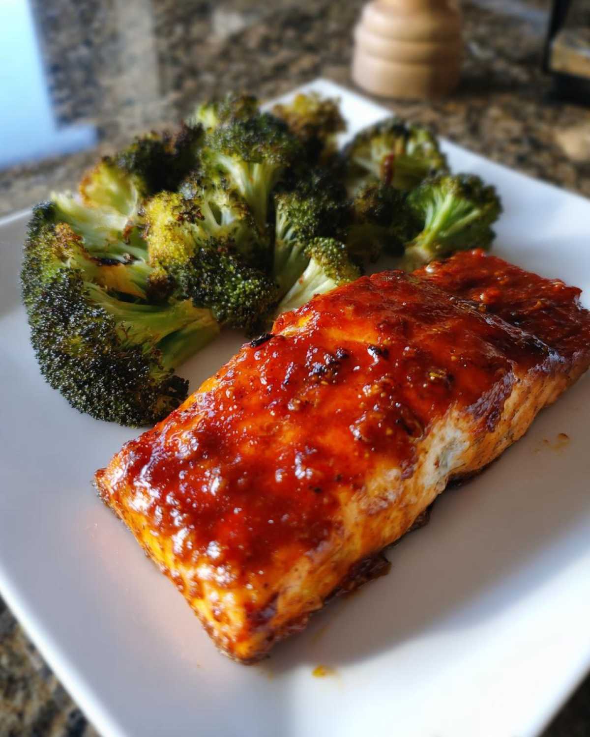 A close-up of a piece of Sheet Pan Honey Harissa Salmon with Broccoli on a white plate.