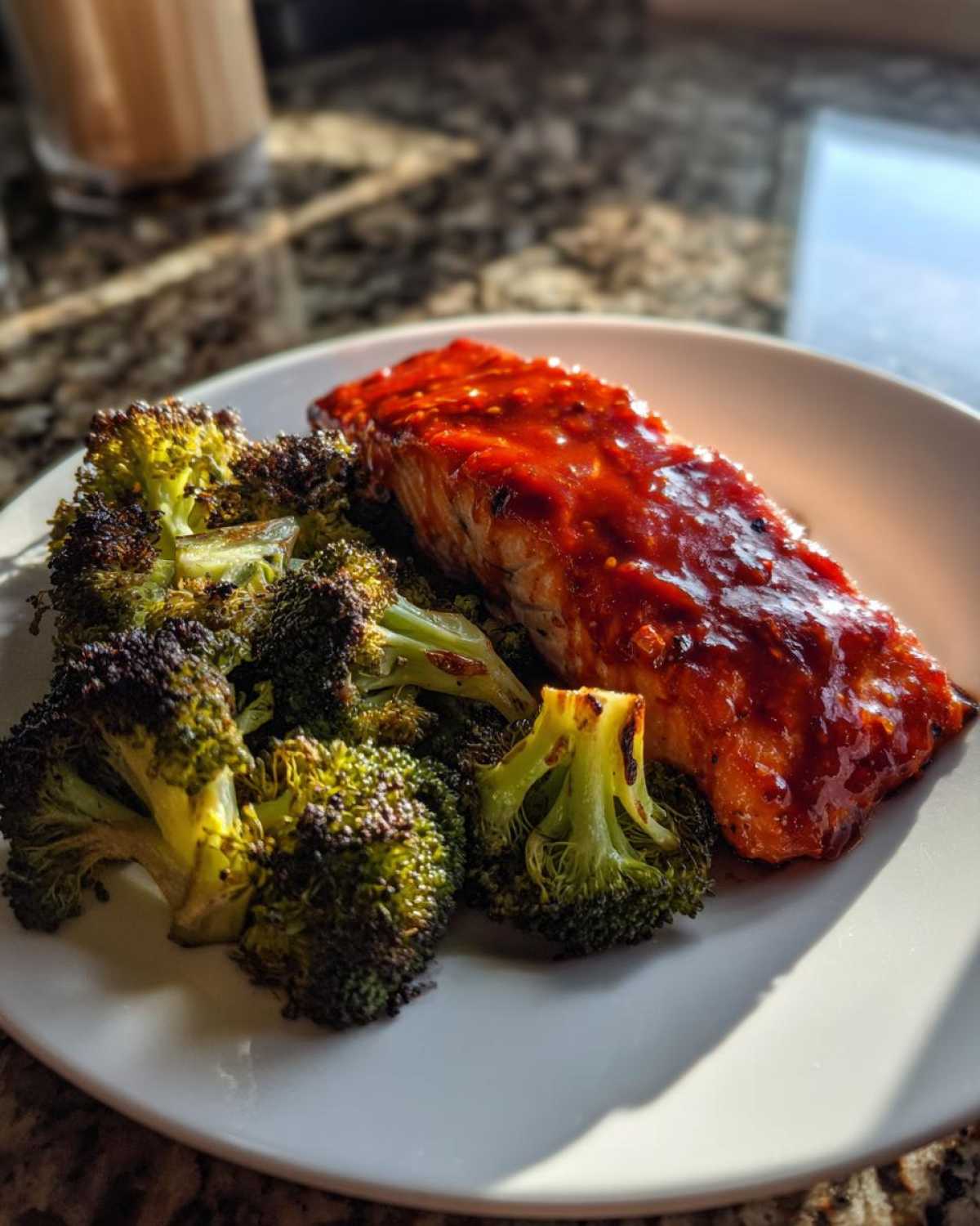 A serving of Sheet Pan Honey Harissa Salmon with Broccoli on a white plate, glistening with sauce.