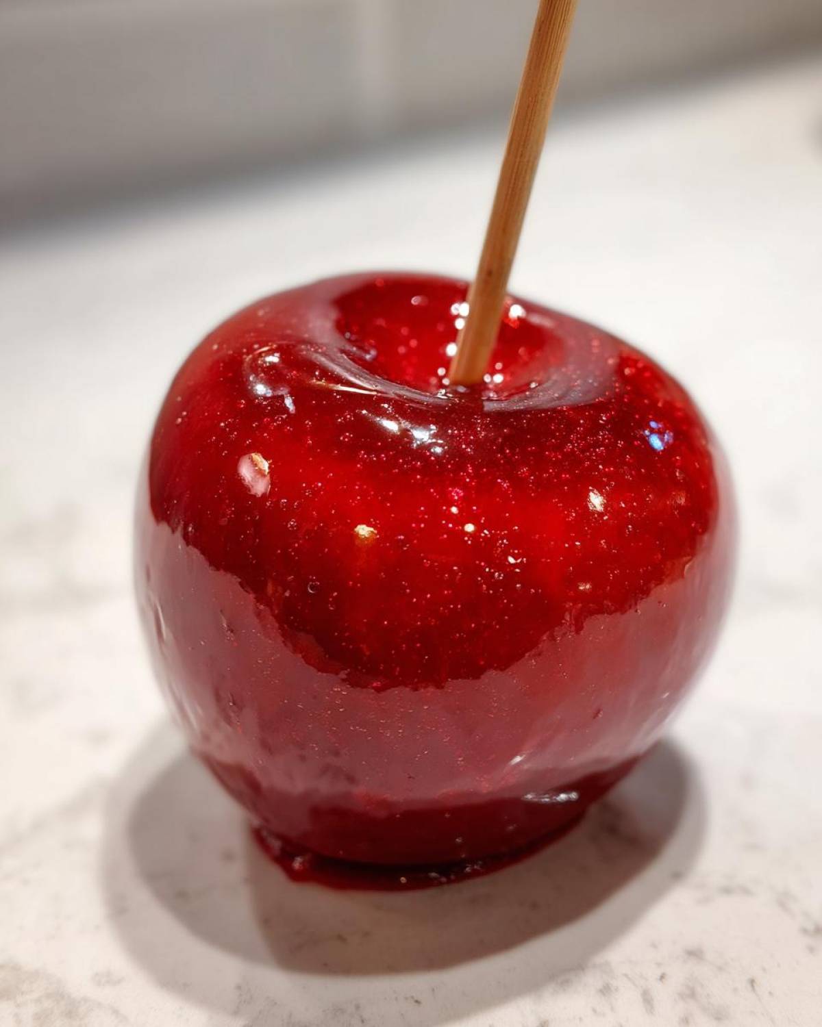 Close-up of a single, perfectly coated, glossy red candy apple with a wooden stick inserted.