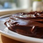 Close-up of rich, glossy chocolate ganache spread thickly over a dessert, showing beautiful swirls.