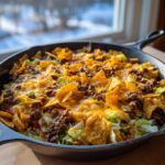 A close-up of Frito Cowboy Cabbage in a cast iron skillet, topped with ground beef, melted cheese, and tortilla chips.