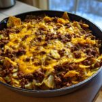 A close-up of Frito Cowboy Cabbage cooked in a black skillet, topped with seasoned ground beef, melted cheddar cheese, and corn chips.