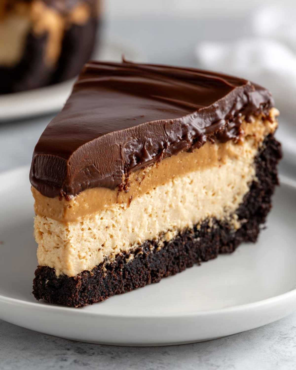 A perfect slice of chocolate peanut butter pie showing a dark crust, creamy peanut butter filling, and chocolate ganache topping.