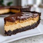 A decadent slice of chocolate peanut butter pie with a dark crust, creamy filling, and glossy chocolate topping.