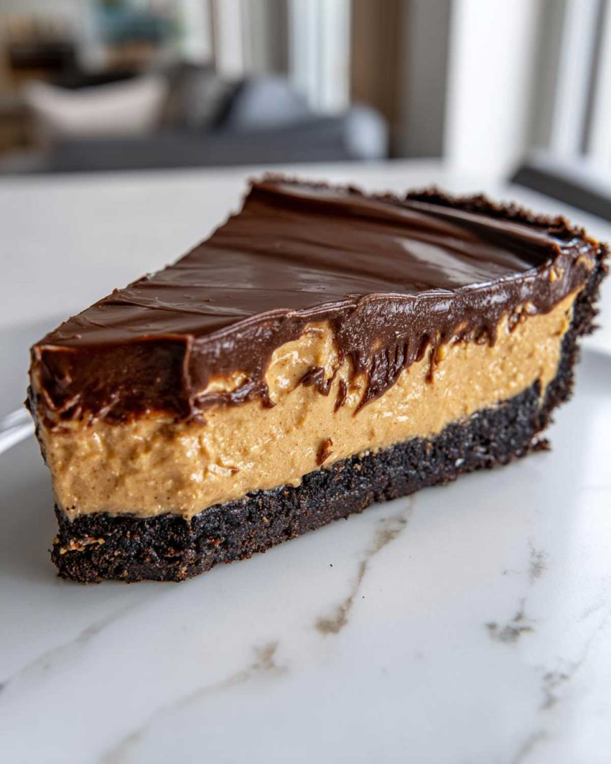 A close-up of a rich slice of chocolate peanut butter pie showing the dark crust, creamy peanut butter filling, and glossy chocolate topping.