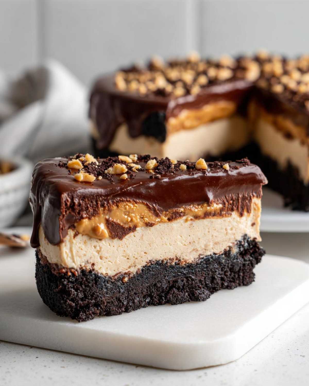 A thick slice of chocolate peanut butter pie showing layers of dark crust, creamy filling, and chocolate ganache topping.
