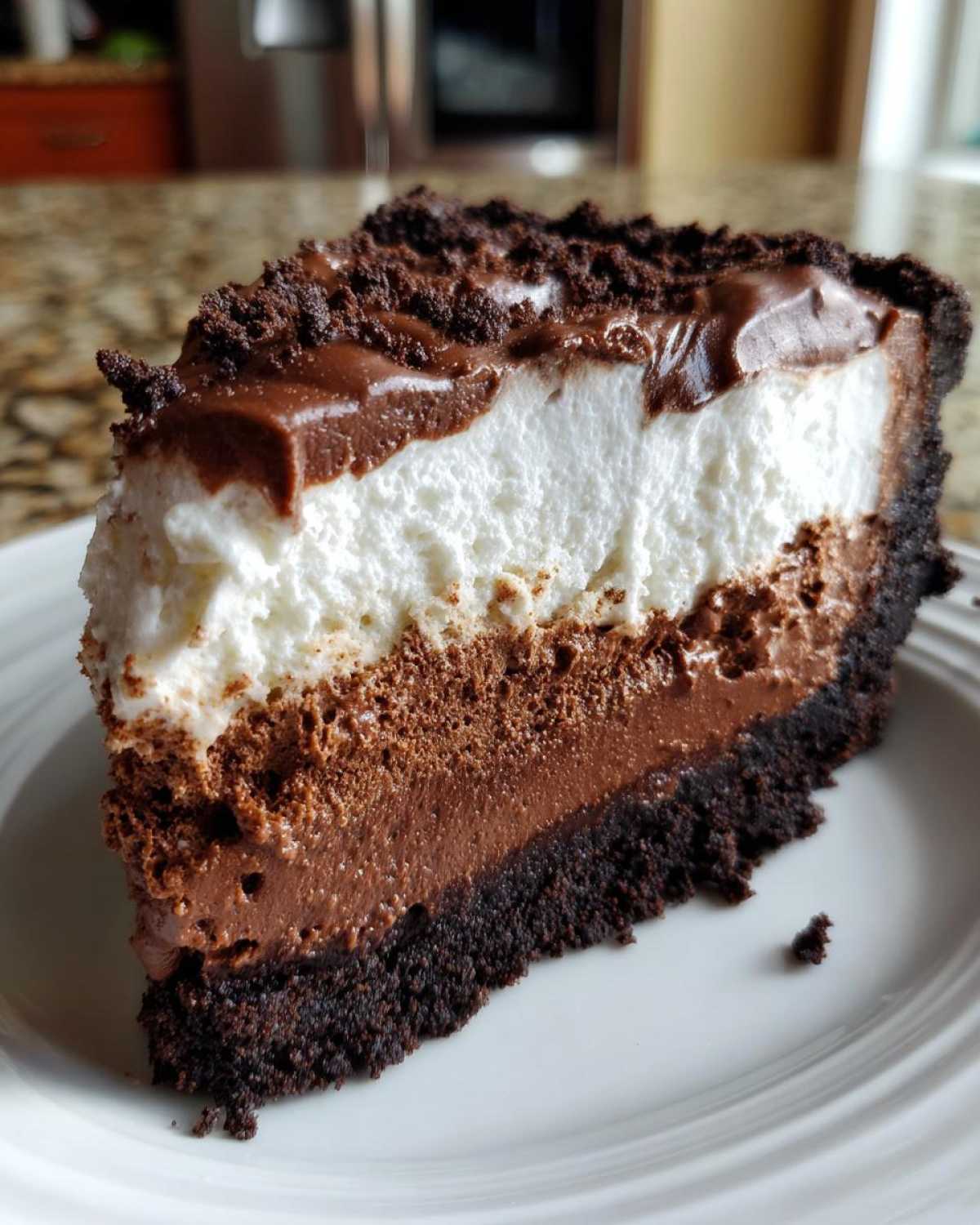 A thick slice of Mississippi Mud Pie showing three distinct layers: dark crust, chocolate mousse, white cream, and chocolate topping.