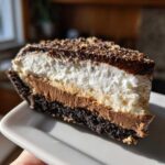 Close-up of a decadent slice of mississippi mud pie showing the dark crust, chocolate layer, white whipped topping, and chocolate drizzle.