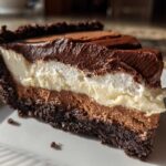A decadent slice of three-layer mississippi mud pie showing a dark crust, chocolate mousse, white cream layer, and chocolate topping.