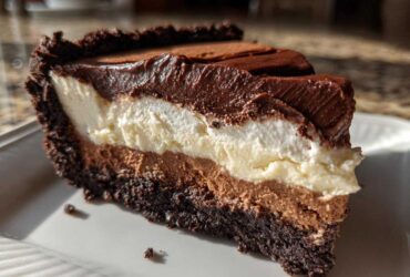 A decadent slice of three-layer mississippi mud pie showing a dark crust, chocolate mousse, white cream layer, and chocolate topping.