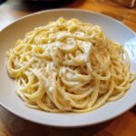 A close-up of spaghetti generously coated in thick, rich Creamy Alfredo Sauce served in a white bowl.