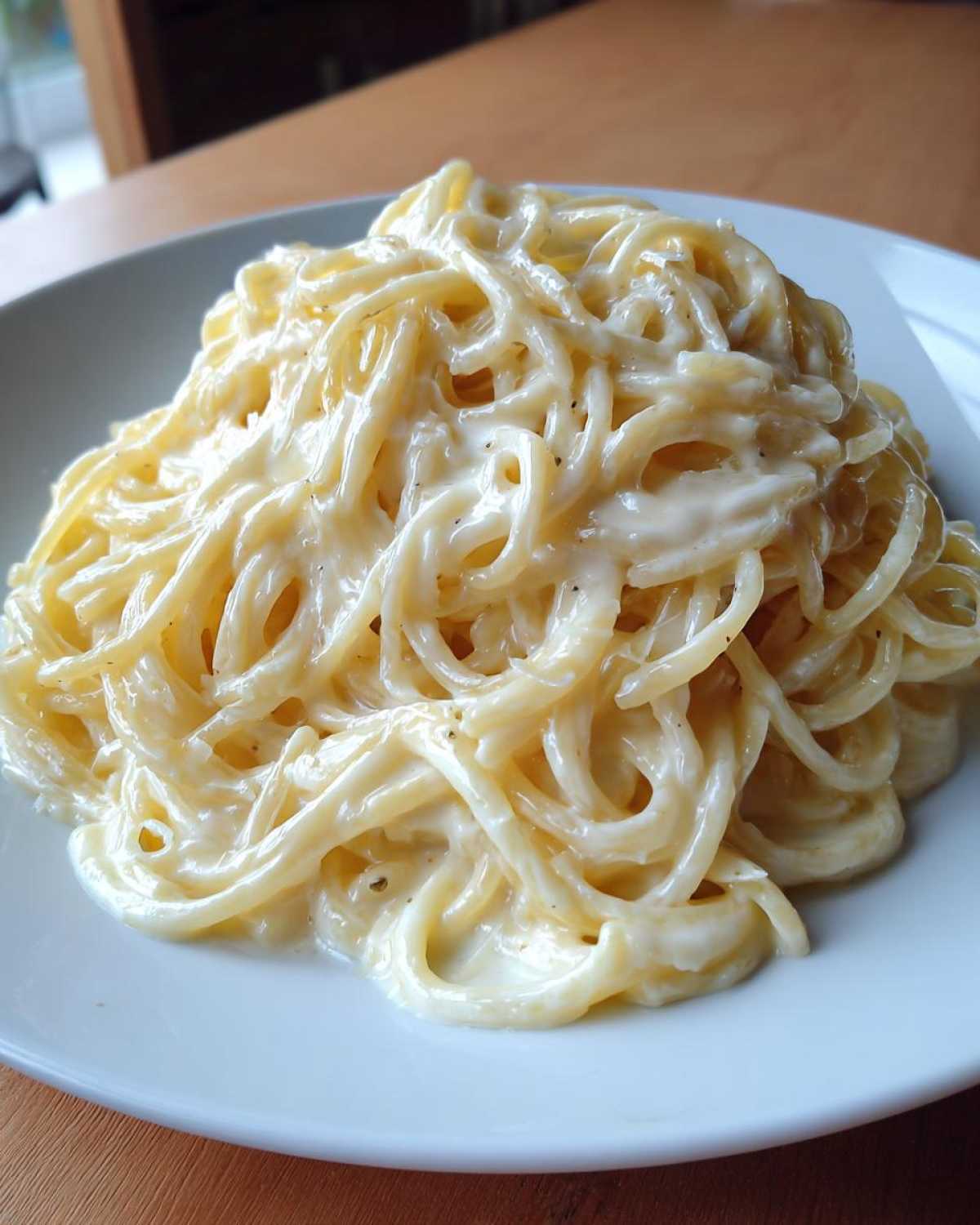Close-up of spaghetti generously coated in rich, white Creamy Alfredo Sauce, served on a white plate.