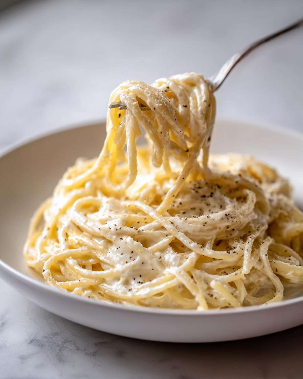 A fork lifting creamy spaghetti coated in Easy Cottage Cheese Alfredo Sauce, topped with black pepper.