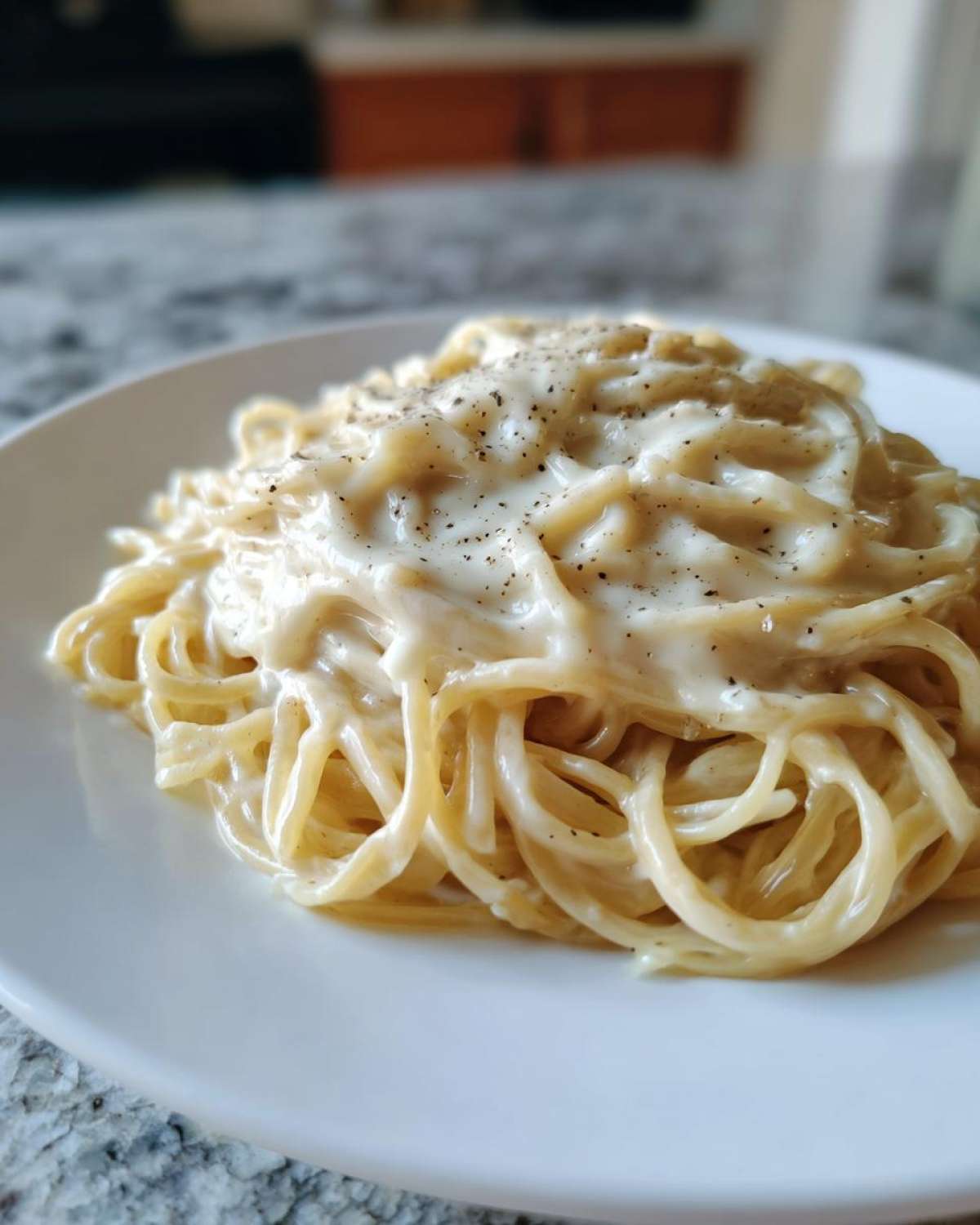 Close-up of spaghetti noodles generously coated in creamy Easy Cottage Cheese Alfredo Sauce and topped with black pepper.