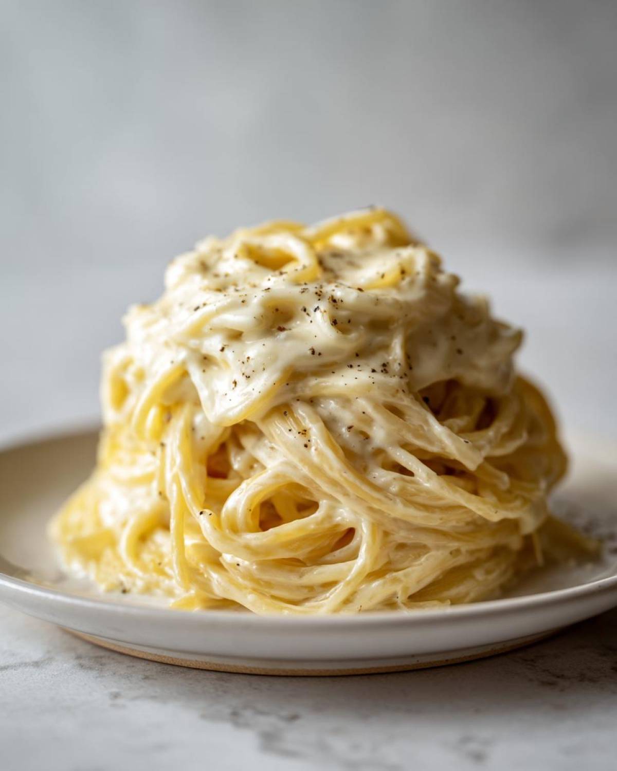A perfectly twirled mound of spaghetti generously coated in creamy Easy Cottage Cheese Alfredo Sauce and topped with black pepper.