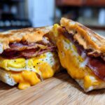 A close-up of a Spicy Chipotle Breakfast Sandwich cut in half, showing melted cheese, fried egg, and bacon.