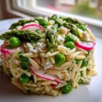 A molded serving of Spring Orzo Pasta Salad featuring asparagus, bright green peas, sliced radishes, and feta cheese.