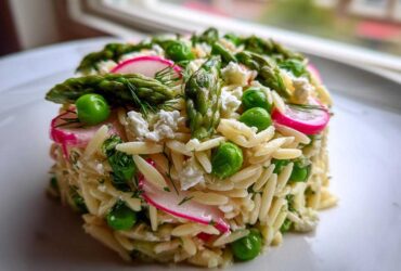 A molded serving of Spring Orzo Pasta Salad featuring asparagus, bright green peas, sliced radishes, and feta cheese.