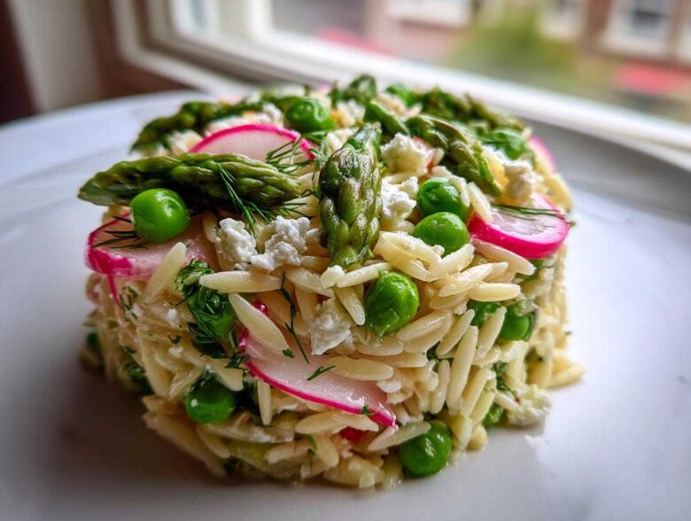 A molded serving of Spring Orzo Pasta Salad featuring asparagus, bright green peas, sliced radishes, and feta cheese.