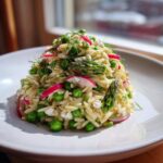 A mound of bright Spring Orzo Pasta Salad featuring orzo, green peas, asparagus tips, radish slices, and feta cheese.