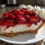 A close-up of a decadent slice of Strawberry Cream Pie featuring a graham cracker crust, thick cream filling, and glossy strawberry topping.
