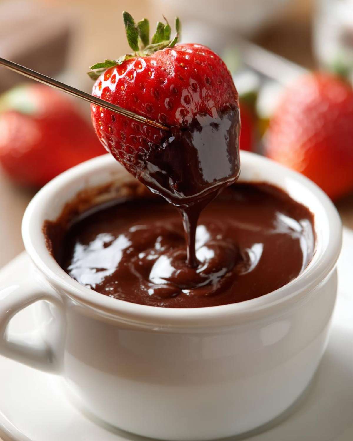 A fresh strawberry being dipped into rich, melted chocolate fondue using a fondue fork.