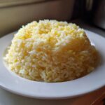 A perfectly molded serving of fluffy Texas Roadhouse Seasoned Rice with visible yellow flecks, served on a white plate.