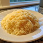 A mound of fluffy, yellow Texas Roadhouse Seasoned Rice served on a white plate.