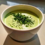 A bright green bowl of Vegan Creamy Cucumber Dill Soup topped generously with fresh dill and chives.