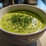 Close-up of a white bowl filled with bright green Vegan Creamy Cucumber Dill Soup, topped with fresh chopped chives.