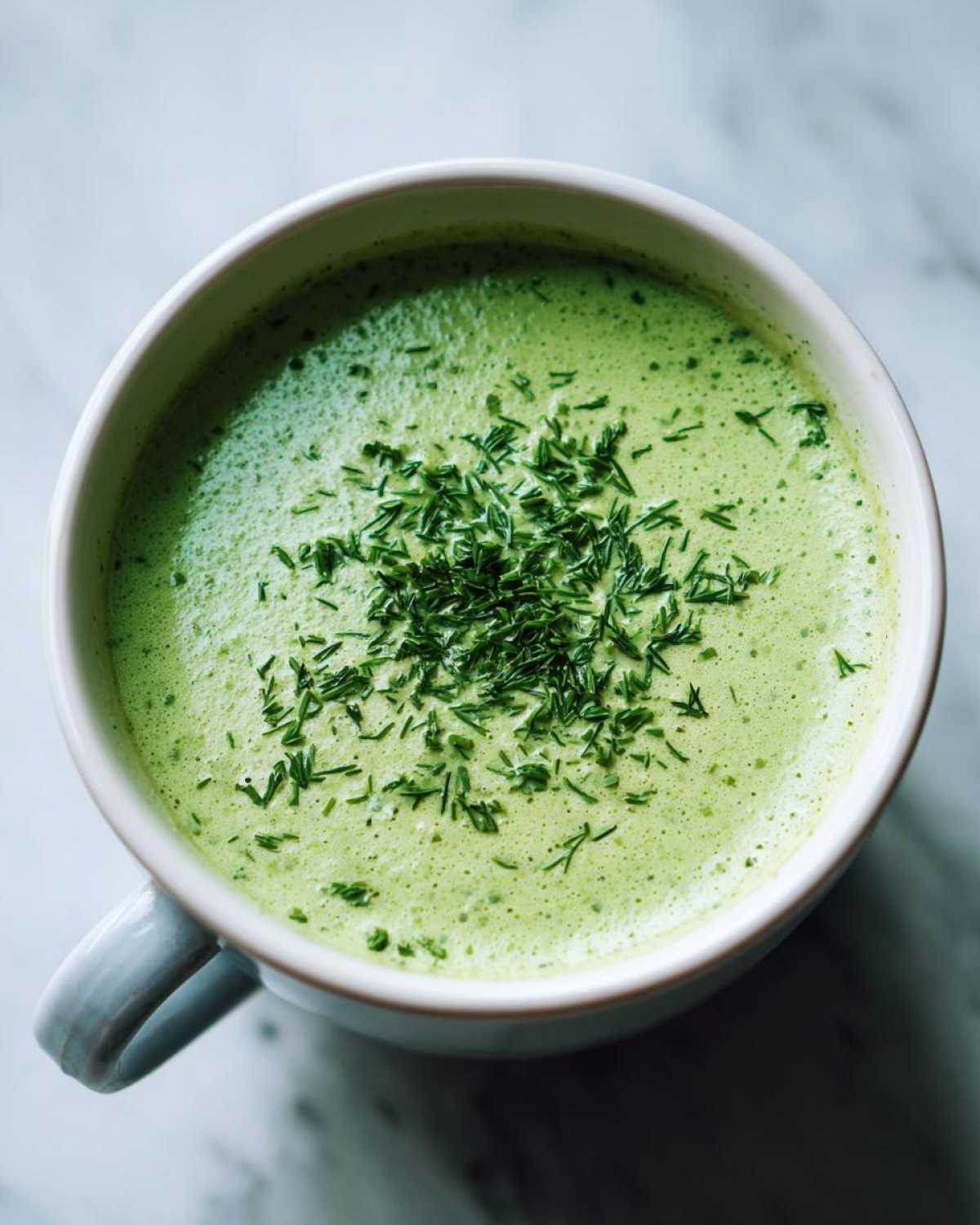 Overhead view of a vibrant green Vegan Creamy Cucumber Dill Soup topped generously with chopped fresh dill.