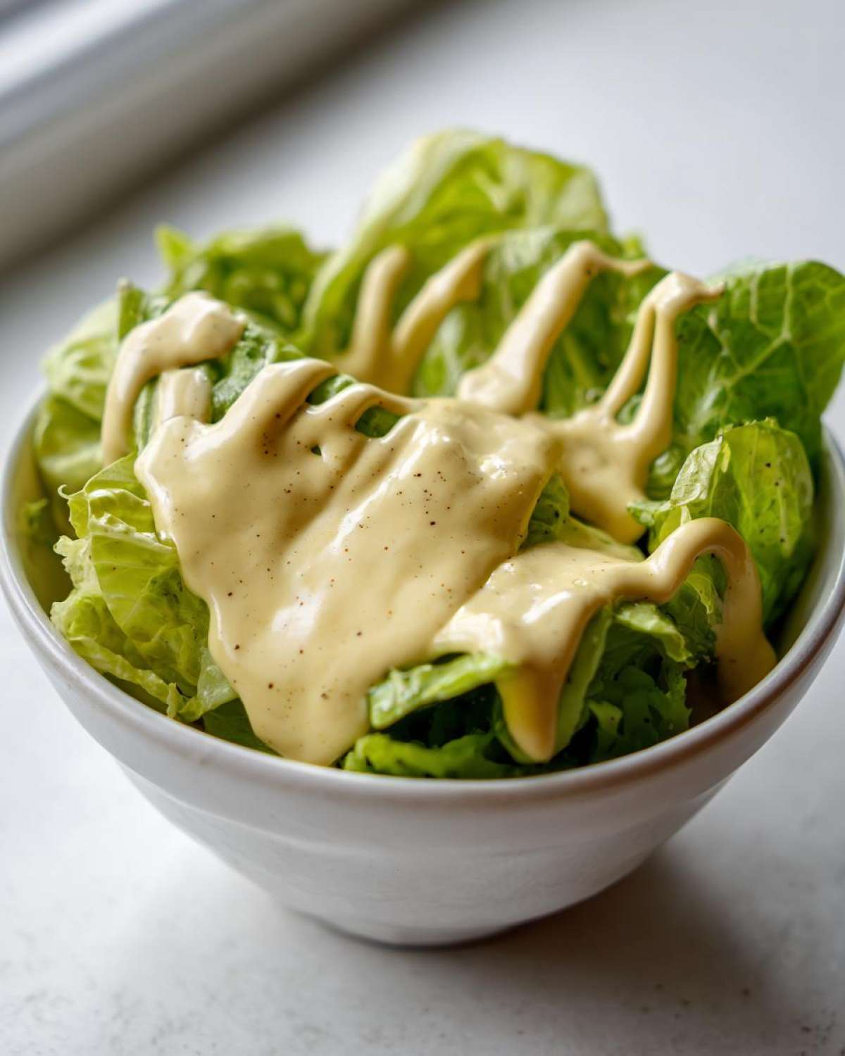 Close-up of fresh lettuce topped with thick Vegan Creamy Lemon Tahini Dressing.