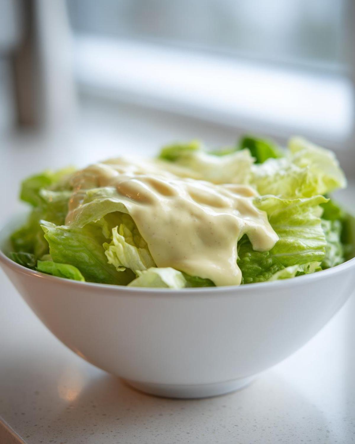 A white bowl filled with crisp lettuce topped generously with Vegan Creamy Lemon Tahini Dressing.